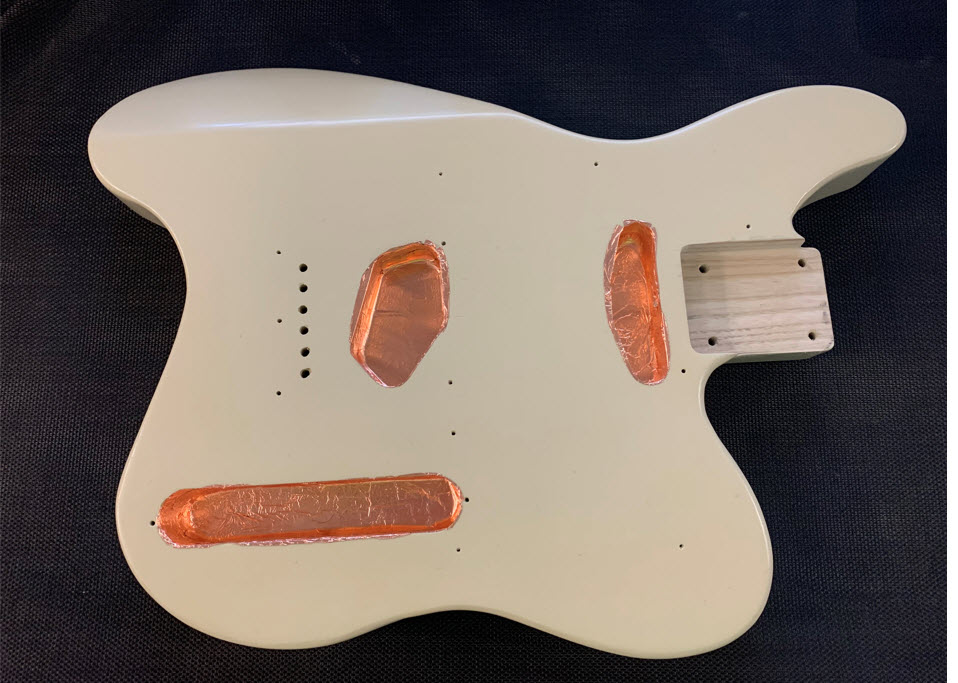 Ergonomic guitar body showing copper tape lining pickup routes and control cavity.