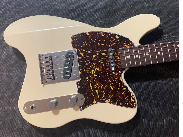 The Wave T ergonomic electric guitar has a cream colored body with a cutout in back, a tortoise shell pickguard and a roasted maple neck. The double cutout is for playing in the classical style.