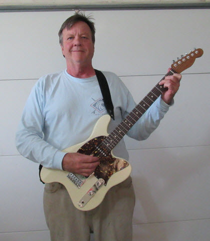 Shows a person playing the ergonomic guitar standing a using a strap.